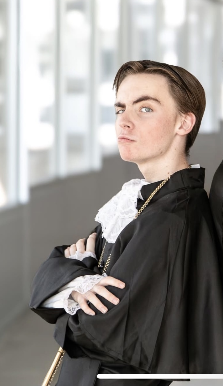 Van in a black robe with lace collar, arms crossed